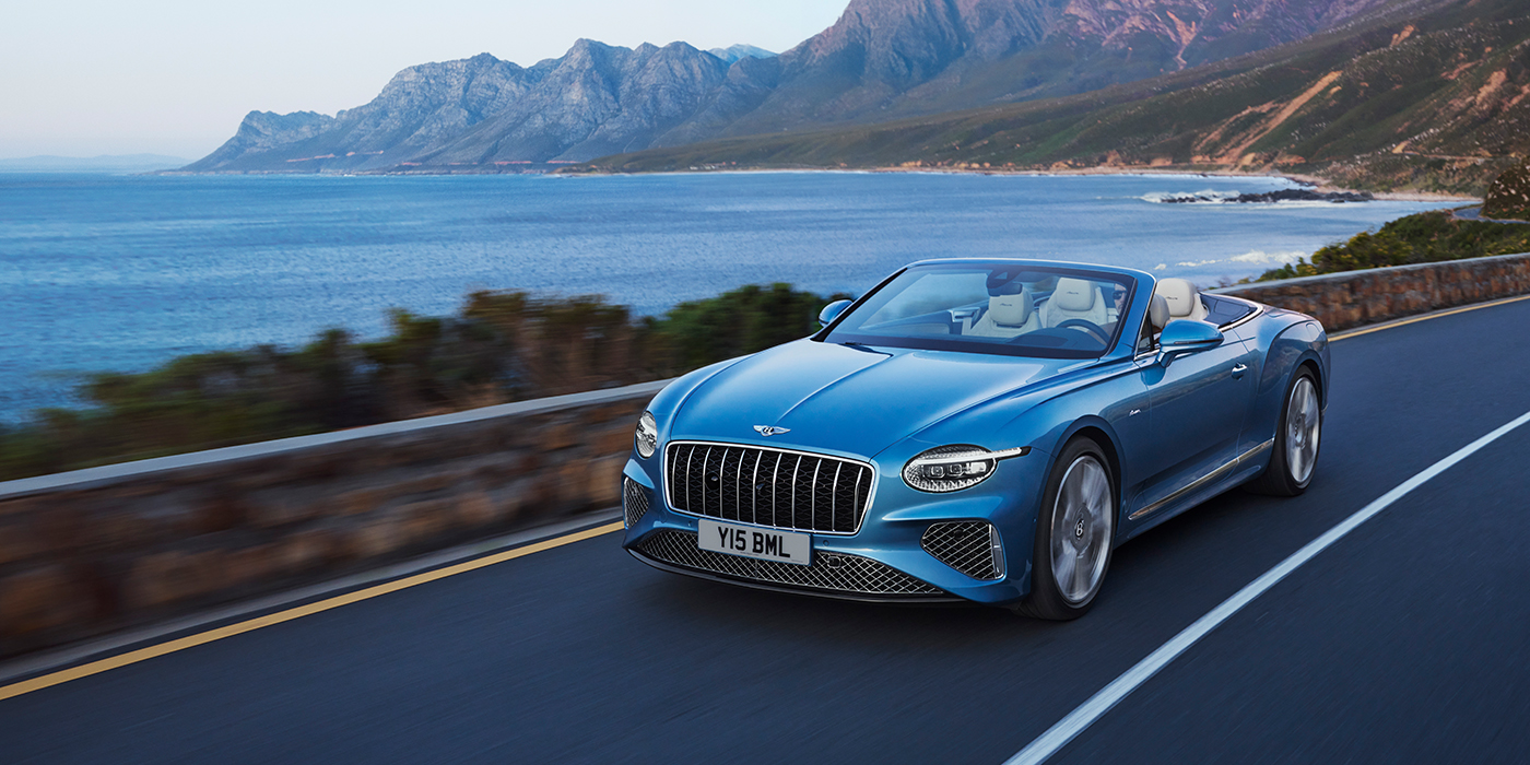 Bentley Tallinn New Bentley Continental GTC Azure convertible in Light Windsor blue paint with 22 inch Azure wheels and chrome grill, driving dynamically by the sea