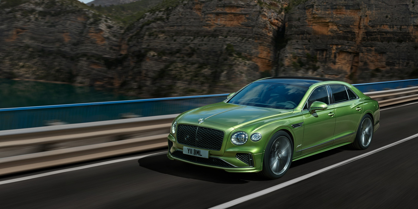 Bentley Tallinn Bentley New Flying Spur Speed v8 hybrid sedan driving dynamically on a mountain road in Tourmaline Green paint