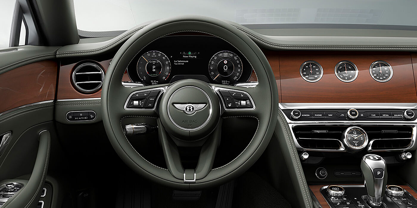 Bentley Tallinn New Bentley Flying Spur sedan front cabin in Cumbrian Green hide and Crown Cut walnut veneer showing steering wheel and Rotating Display with three clocks on face