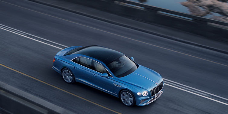 Bentley Tallinn New Bentley Flying Spur Azure sedan in Light windsor blue paint by Mulliner, with 22 inch Azure wheels seen from overhead driving dynamically on a country road