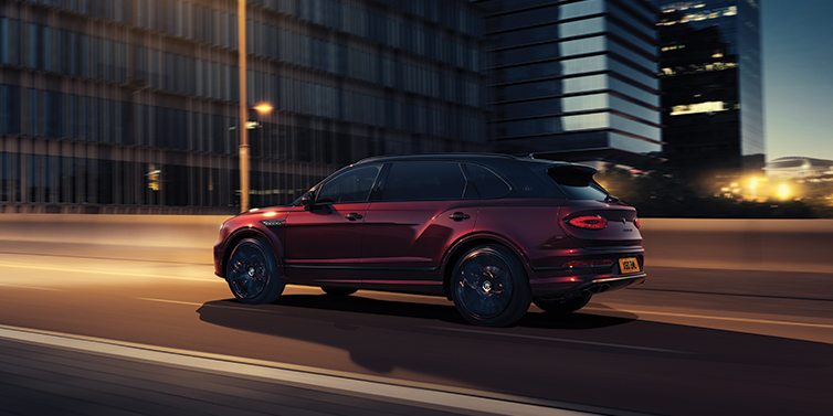 Bentley Tallinn Bentley Bentayga Extended Wheelbase Mulliner SUV in Cricket Ball red paint driving dynamically in city at night