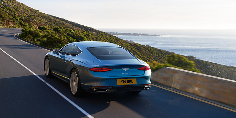 Bentley Tallinn New Bentley Continental GT Azure coupe in Light Windsor blue paint seen from the rear driving dynamically on a seaside road