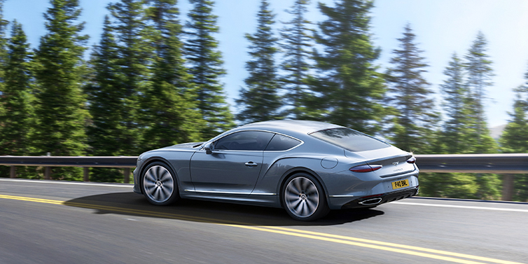 Bentley Tallinn New Bentley Continental GT coupe in Silverlake paint, seen from the rear, driving dynamically on a tree-lined road