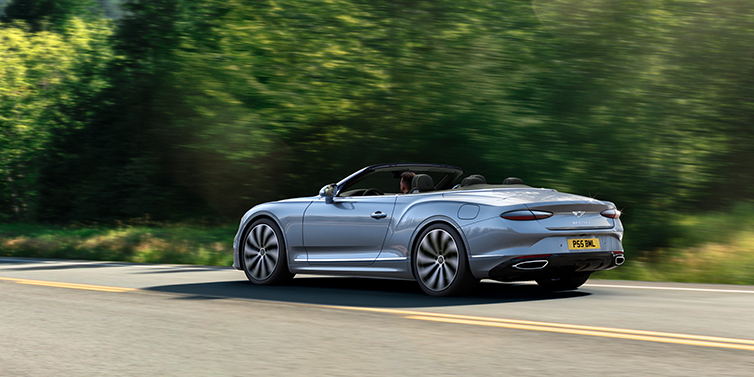 Bentley Tallinn New Bentley Continental GTC convertible side view in Silverlake paint with 22 inch ten spoke wheels driving dynamically on a country road